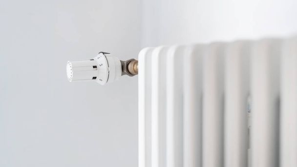白の近代的なアパートで中央暖房システムのラジエーター付きのWebバナー。部屋の温度を調整するためのレギュレータノブに選択的な焦点を当てます。エネルギー消費の概念 - 写真・画像