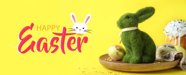 Wielkanocna kartka z zabawkowym króliczkiem, jajkami i ciastkami na żółtym tle  - Zdjęcie, obraz
