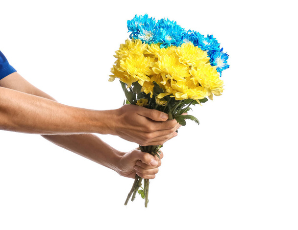 Αρσενικά χέρια κρατώντας μπουκέτο από λουλούδια βαμμένα σε χρώματα της ουκρανικής σημαίας σε λευκό φόντο - Φωτογραφία, εικόνα
