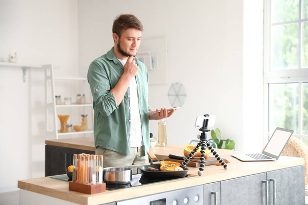 Nachdenklicher junger Mann mit Tablet-Computer schaut sich Kochvideo-Anleitung in Küche an - Foto, Bild