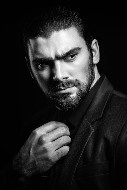 Black and white male portrait. A man in a black classic suit in a black shirt and tie over a black background. Dark-haired young man. - Φωτογραφία, εικόνα