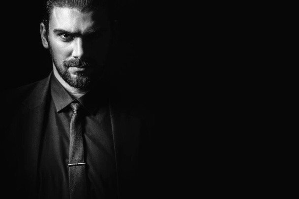 Ritratto maschile in bianco e nero. Un uomo in abito classico nero con camicia nera e cravatta su sfondo nero. Giovane dai capelli scuri. - Foto, immagini