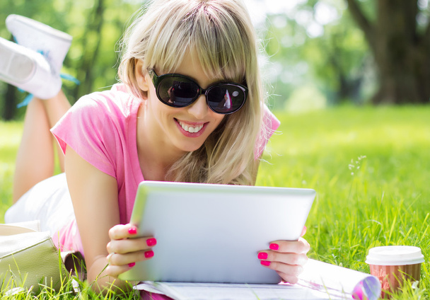 Розслаблена молода жінка використовує планшетний комп'ютер на відкритому повітрі
 - Фото, зображення