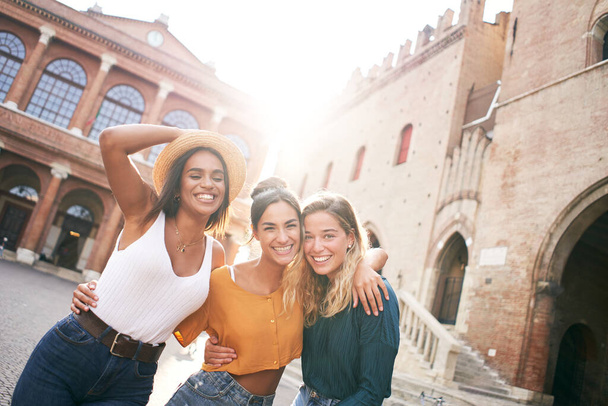 Τρεις χαρούμενες φίλες διασκεδάζουν έξω στις καλοκαιρινές διακοπές στην πόλη. Πορτρέτο της χαμογελαστής γυναίκας αγκαλιάζει κοιτάζοντας κάμερα μαζί - Φωτογραφία, εικόνα