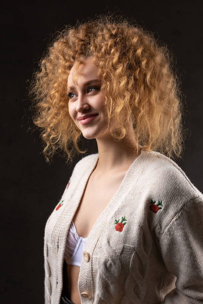 Портрет молодой рыжеволосой кудрявой сексуальной девушки в куртке с длинными волосами в студии. Показывает свою изогнутую грудь в лифчике. - Фото, изображение
