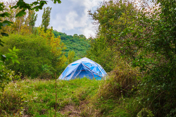 Niebieski namiot turysty w przyrodzie pokryty jest materiałem olejowym lub folią polietylenową. Dodatkowa ochrona przed zamoknięciem podczas pory deszczowej. Tło z przestrzenią do kopiowania - Zdjęcie, obraz
