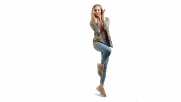 zaskoczony piękny europejski blondynka dziewczyna z jedną stopą w górę trzymając ręce wyciągnięte i uśmiechając się do kamery full shot studio strzał biały tło - Materiał filmowy, wideo