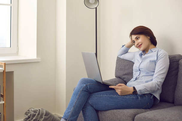Smiling millennial woman looking at laptop screen relax on couch at home - Fotó, kép