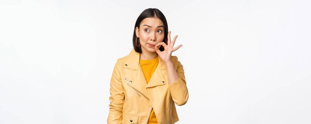 Image of young asian woman seal lips, silence gesture, zipping her mouth with promise, standing over white background - Photo, Image