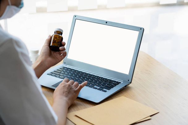 Doctor holding a pill bottle and typing on a laptop keyboard. The hand of a doctor or nurse writing a prescription at the medical office. health care and health check concept - Foto, Bild