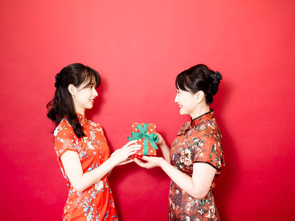 Daughter wearing traditional cheongsam qipao is congratulating mom and giving present wrapped in gift box. Family holiday and togetherness. - Fotó, kép