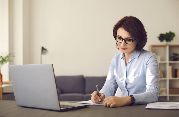 Millennial caucasian woman study on laptop making notes at home office - Valokuva, kuva