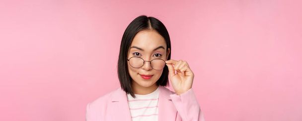 Porträt einer asiatischen Geschäftsfrau mit Brille, die fasziniert in die Kamera blickt und lächelt, professionelle Verkäuferin, die interessiert anstarrt, rosa Hintergrund - Foto, Bild