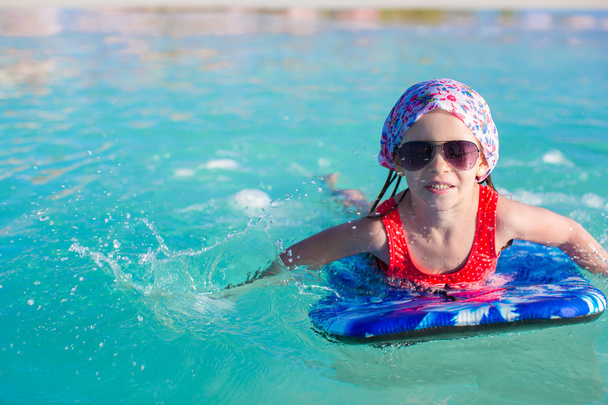 kleines entzückendes Mädchen auf dem Surfbrett im türkisfarbenen Meer - Foto, Bild