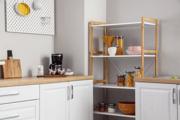 Moderne Regaleinheit und Theke mit Kaffeemaschine in der Nähe der Lichtwand in der Küche - Foto, Bild