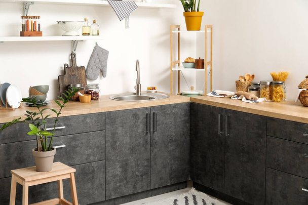 Wooden counters with sink, houseplant and different cookware near white wall - 写真・画像