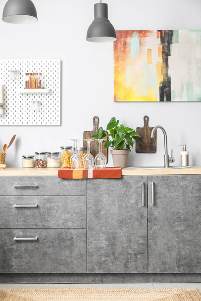 Comptoir en bois avec évier en argent, plante d'intérieur, savon à vaisselle et ustensiles de cuisine près du mur blanc - Photo, image