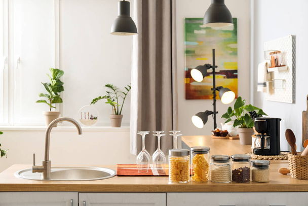 Houten toonbank met zilveren spoelbak, glazen en potten in lichte keuken - Foto, afbeelding