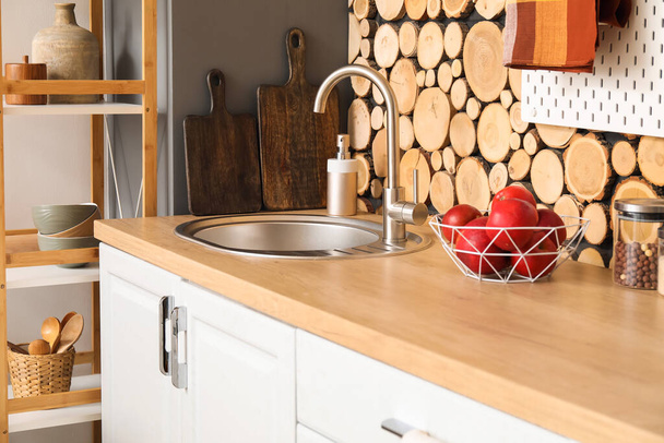 Licznik ze srebrnym zlewem, kosz jabłek, desek i mydła w pobliżu drewnianej ściany w kuchni - Zdjęcie, obraz