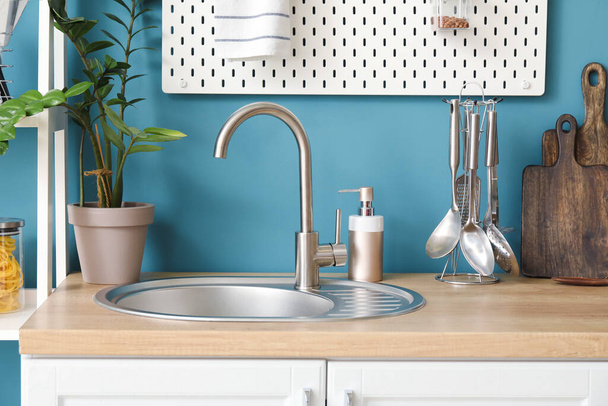 Gümüş lavabolu ahşap tezgah, yemek takımı, ev bitkisi ve mutfak mavi duvarının yanında bulaşık deterjanı. - Fotoğraf, Görsel