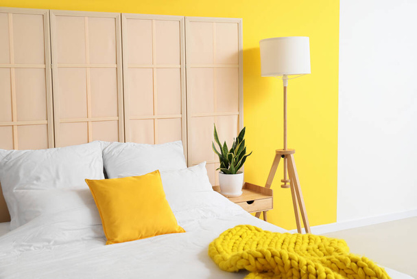 Удобная кровать, современная лампа и складной экран рядом с цветной стеной - Фото, изображение