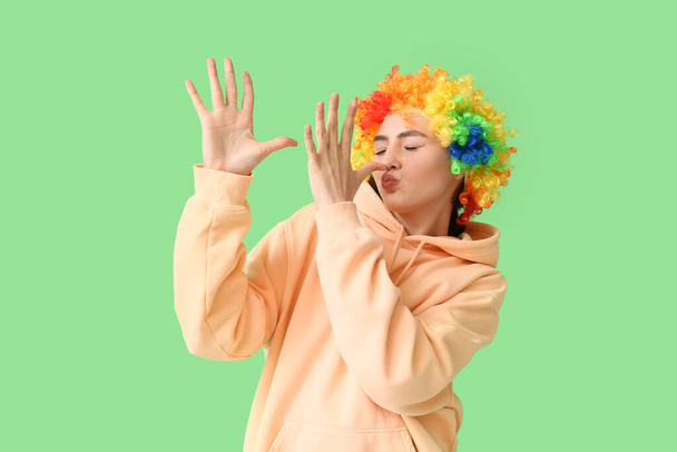 Mujer joven divertida en peluca colorida sobre fondo verde. Celebración del Día de los Inocentes - Foto, imagen