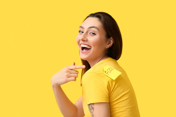 Mujer risueña con una nota pegajosa en la espalda sobre un fondo amarillo. Día de los tontos de abril - Foto, imagen
