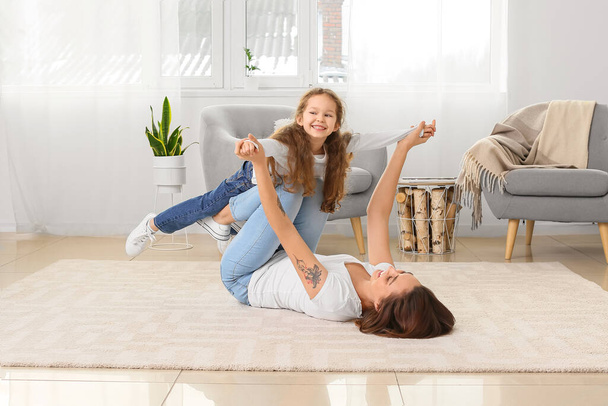 Jonge moeder en haar dochtertje hebben plezier op tapijt thuis - Foto, afbeelding