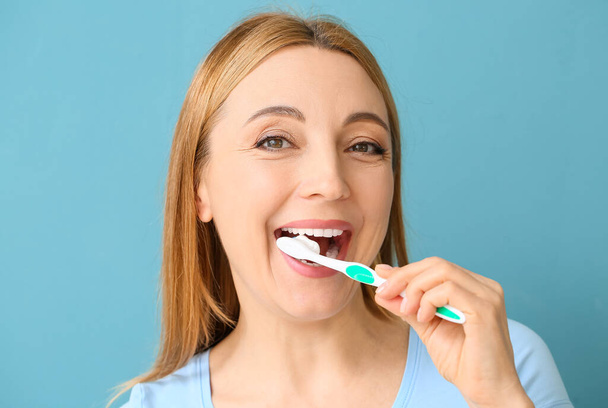 Красивая зрелая женщина чистит зубы на синем фоне - Фото, изображение