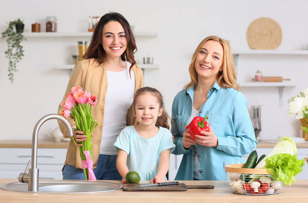 Ευτυχισμένη νεαρή γυναίκα, η μικρή της κόρη και η μητέρα της στην κουζίνα στο σπίτι. Παγκόσμια Ημέρα της Γυναίκας - Φωτογραφία, εικόνα