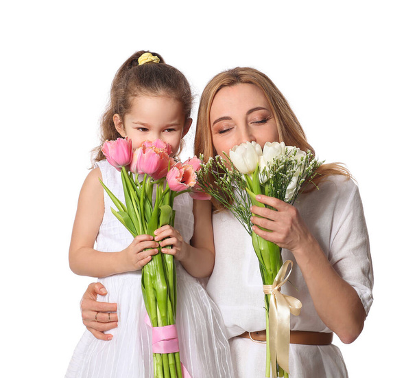 Mature woman and her little granddaughter with flowers on International Women's Day on white background - Photo, Image