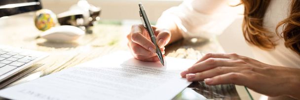 Close-up Of Businesswoman's Hand Signing Contract With Pen Over Desk In Office - Foto, imagen