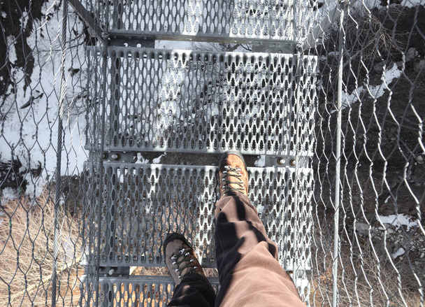 two hiking boots of the hiker as he crosses the suspension bridge in the void - Photo, Image