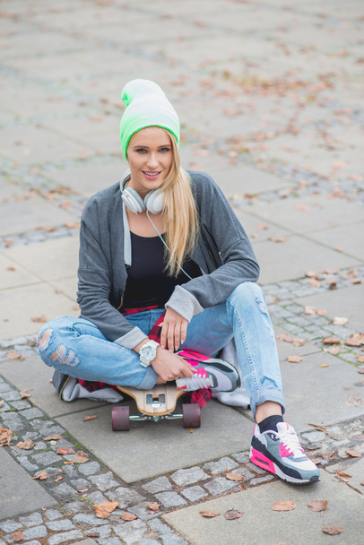Woman in Trendy Attire Sitting Over Skateboard - Photo, Image