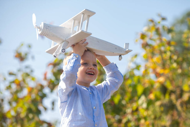 Dreams of flight. Child playing with toy plane against the sky. Dreams of travels. Little dreaming child with a toy airplane plays outdoors. Blonde kid, smiling emotion face. - Foto, imagen