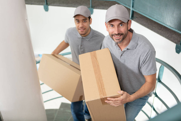 deliverymen holding cardboard boxes in the stairs - Foto, Bild