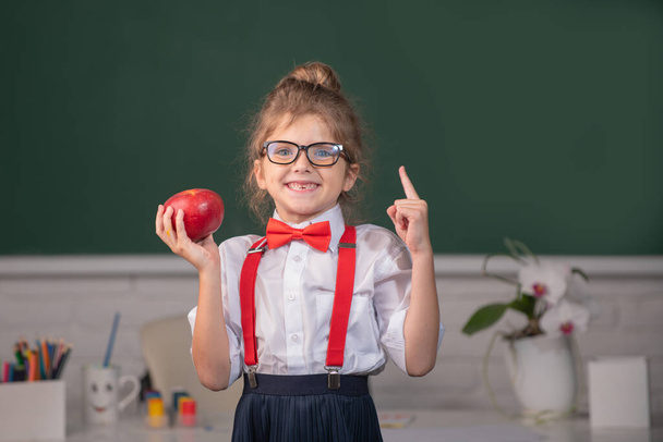 Portrait of school girl nerd student hold apple with surprising expression pointing with finger against blackboard. First day at school. - Foto, Bild