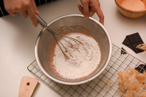 Vista superior, hembra usando un batidor para remover la harina de galletas con una masa de galletas de chocolate en el tazón de mezcla. Mujer cocinando galletas. - Foto, Imagen