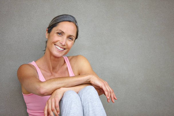 Living a healthy lifestyle. Portrait of an attractive mature woman in gymwear sitting against a gray wall. - Photo, Image