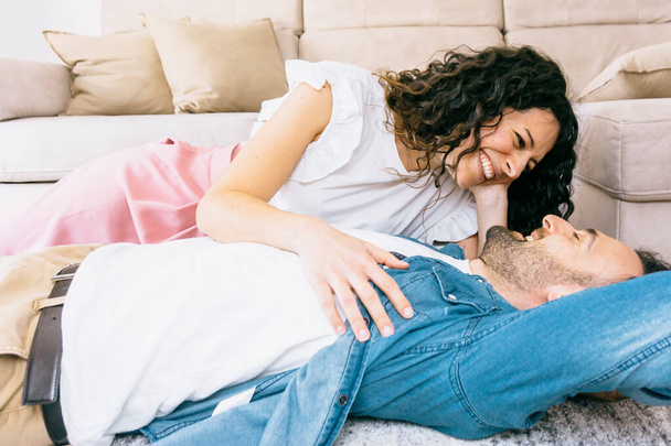 Portrait of a young couple in love hugging while lying on the carpet of their new home - millennial people relax in the living room - Photo, Image