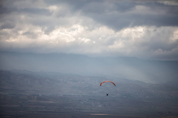 Obrázek paraglidisty letícího sám proti šedé oblačné obloze. - Fotografie, Obrázek