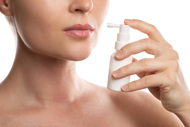 Frau verwendet Spray mit Schmerzmittel zur Linderung von Halsschmerzen auf weißem Hintergrund - Foto, Bild
