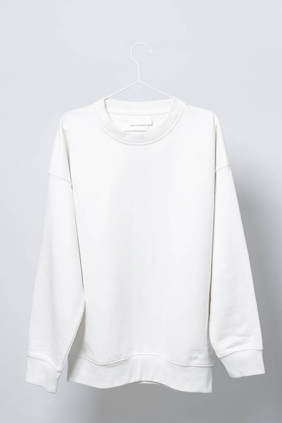 Blank white sweatshirt hanging on the thin metallic hanger against light gray background - Zdjęcie, obraz