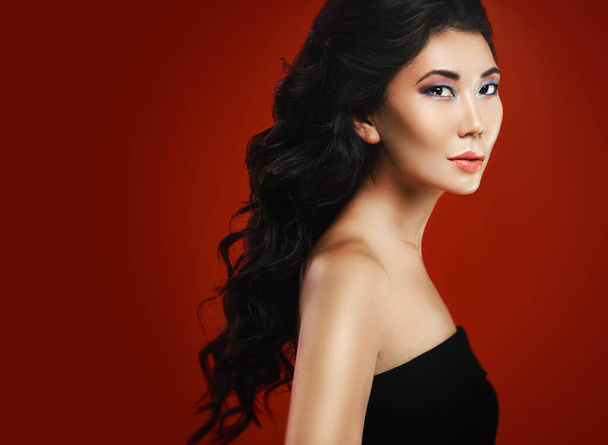 Portrait of stunning asian woman with a beautiful curly hair and make-up over red background - Photo, image