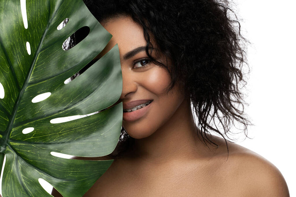 Beautiful black woman with a smooth skin holding green tropical leaf on white background - Foto, afbeelding