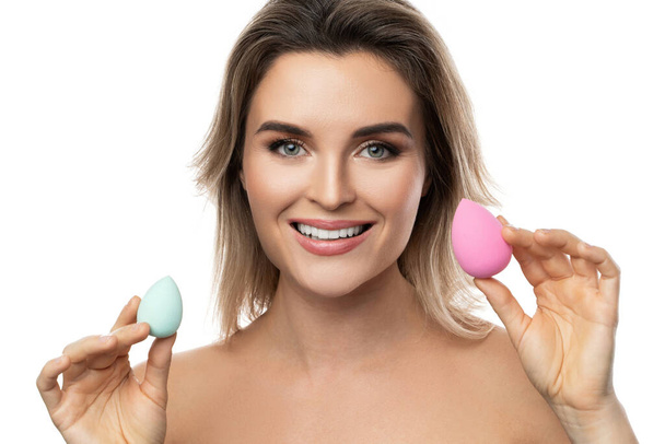 Portrait of beautiful woman with a smooth skin holding makeup sponges on white background - Foto, Bild