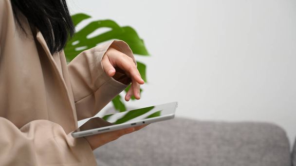 Vista trasera, hembra en un traje casual mínimo usando tableta digital con computadora táctil en la sala de estar. - Foto, Imagen