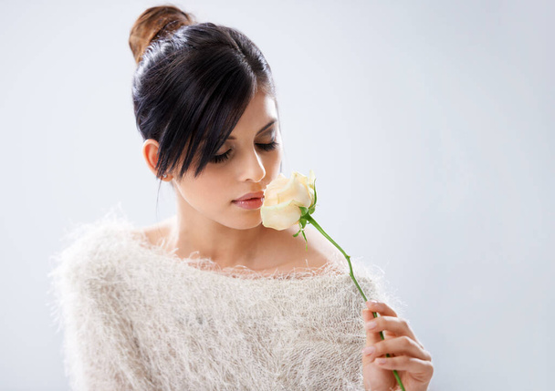Experience natural beauty. A young woman sitting in a studio holding a white rose. - Fotó, kép