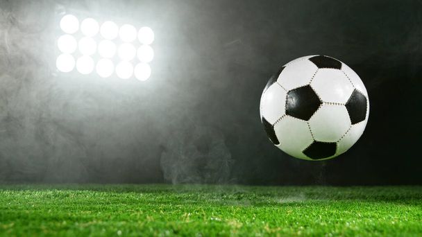 Soccer ball placed on grass, dark background with spotlights. - Фото, изображение