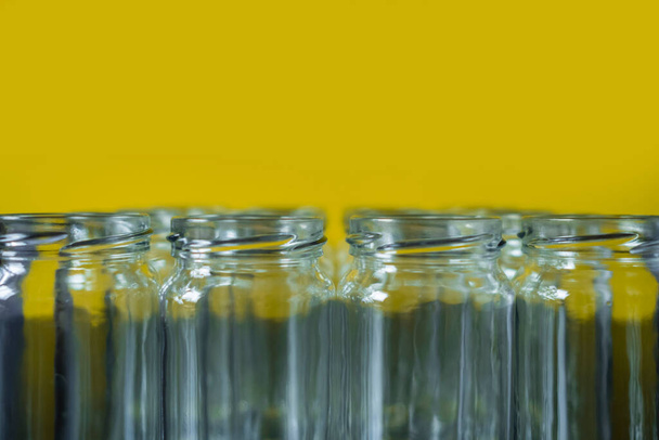 Vue frontale de bocaux en verre vides alignés en rang sur un fond jaune. - Photo, image